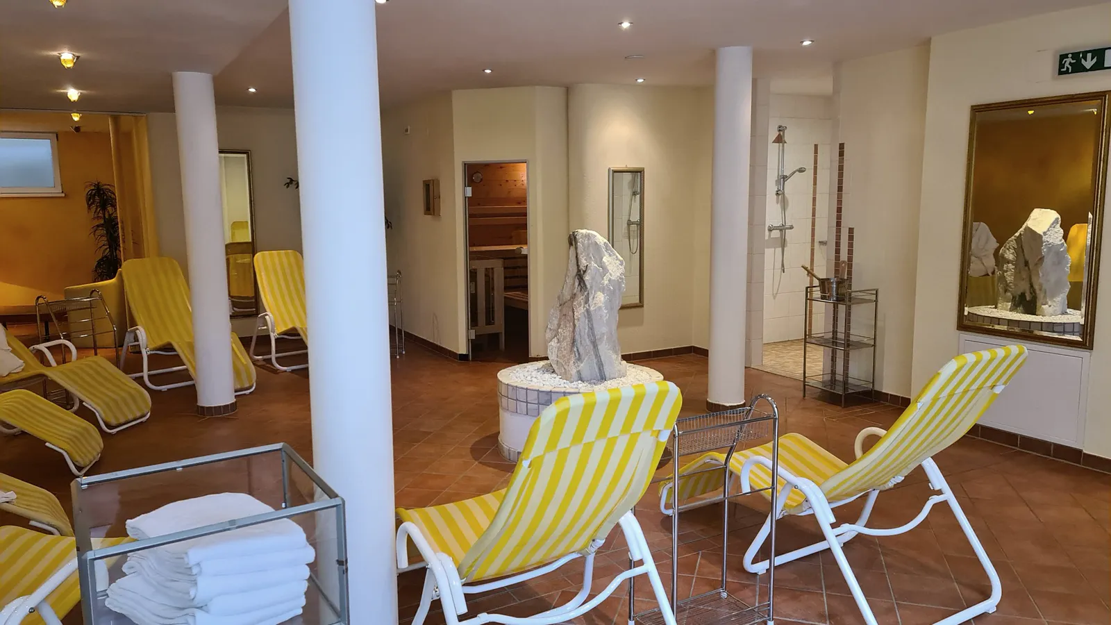 Relaxation room with yellow-striped loungers, stone fountain and sauna door